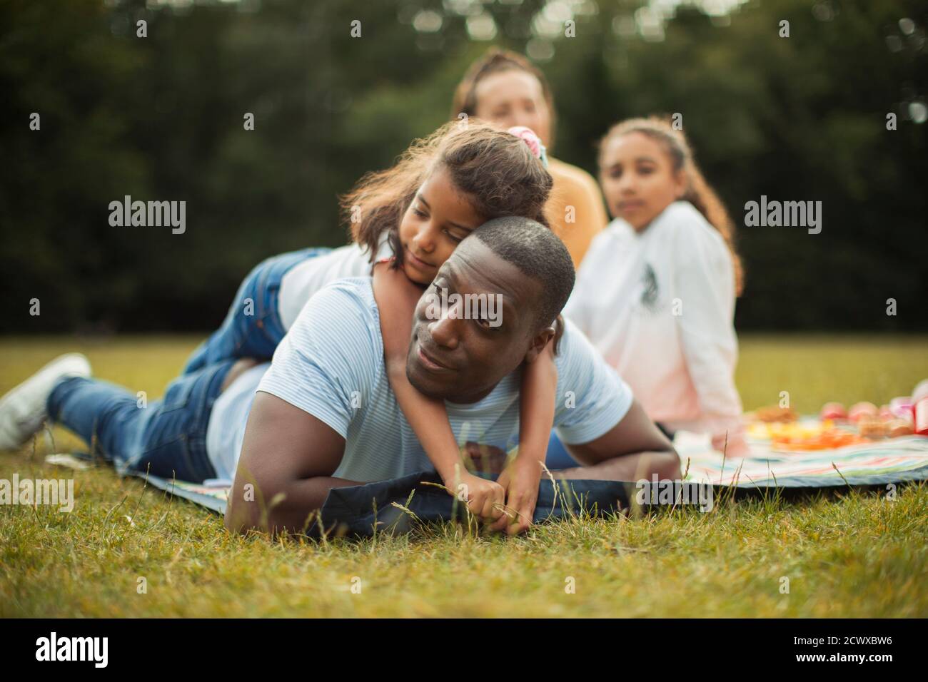 Hija cariñosa abrazando a padre en una manta de picnic en el parque Foto de stock