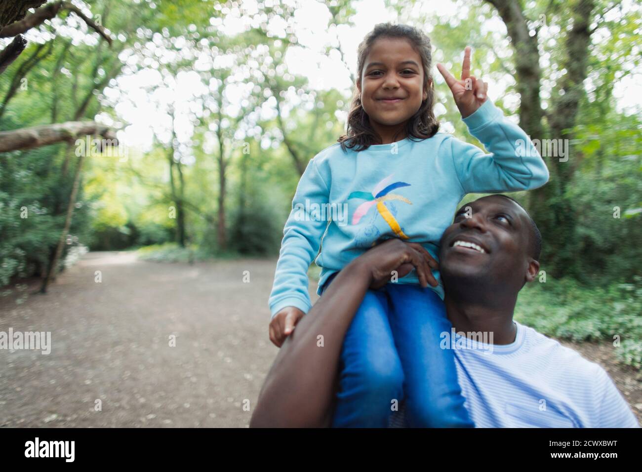 Retrato padre llevando a la hija gestuando signo de paz en el bosque Foto de stock