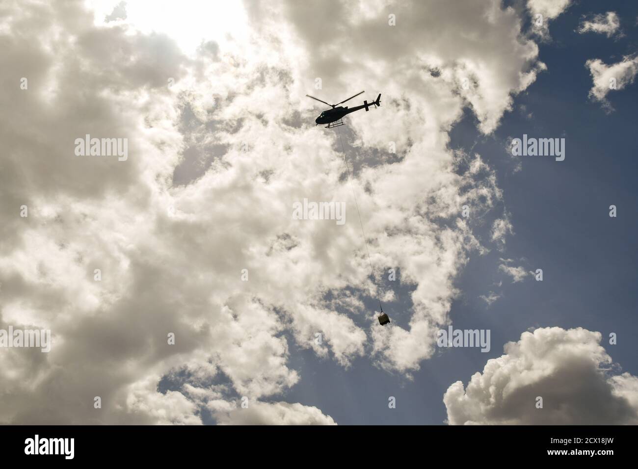 Vista de contraluz de la silueta de un helicóptero que transporta la carga contra el cielo nublado, Courmayeur, Valle de Aosta, Italia Foto de stock