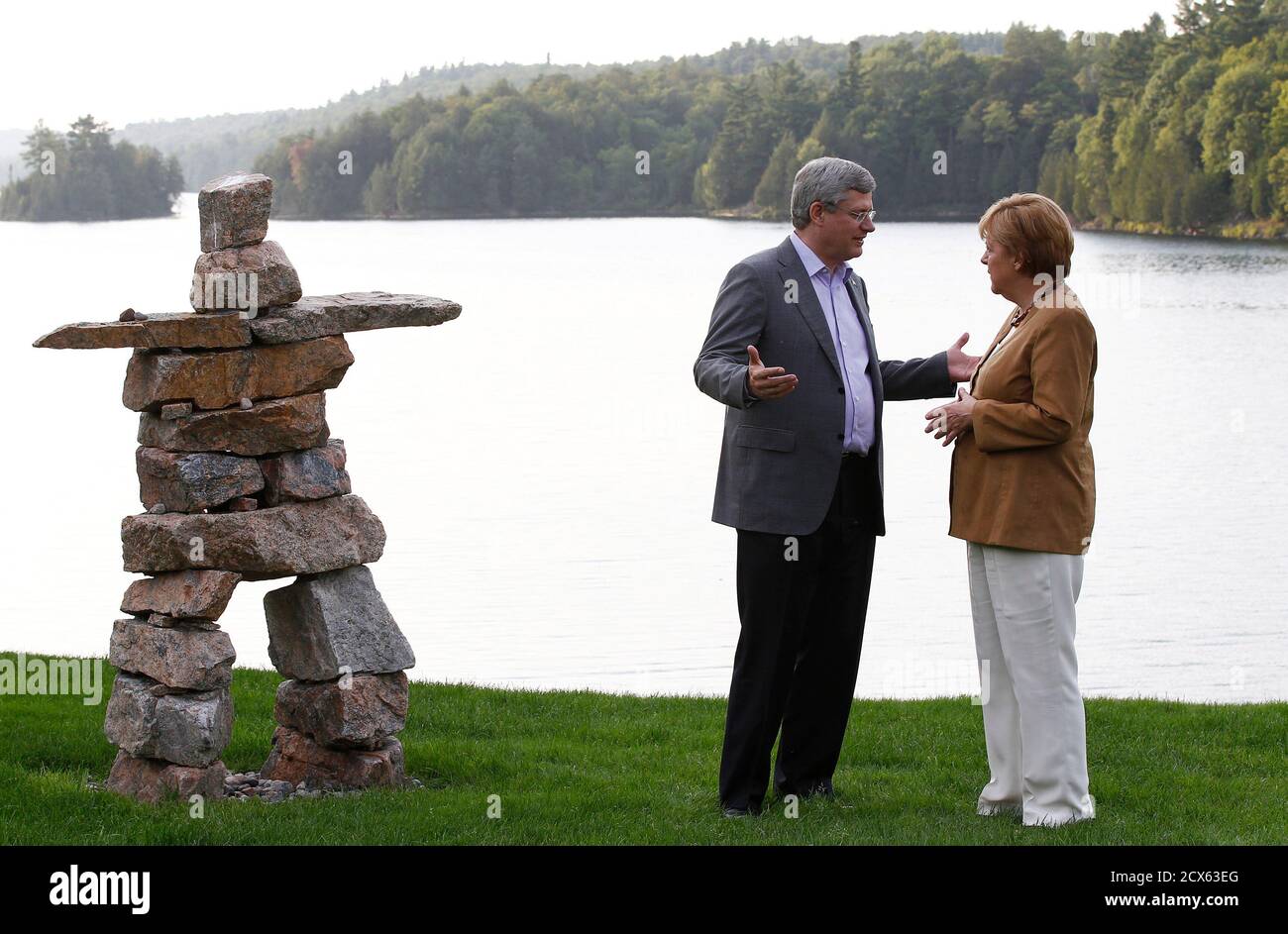 El primer ministro de Canadá, Stephen Harper (L), habla con la canciller alemana, Angela Merkel, en Harrington Lake, retiro oficial de Harper, en Gatineau Park, Quebec, 15 de agosto de 2012. Merkel está en una visita oficial a Canadá del 15 al 16 de agosto. En la foto a la izquierda se encuentra un monumento tradicional de piedra inuit inukshuk. REUTERS/Chris Wattie (CANADÁ - TAGS: POLÍTICA TPX IMÁGENES DEL DÍA) Foto de stock