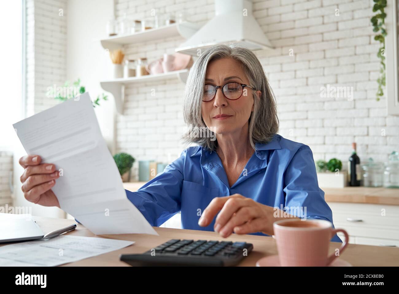 Mujer madura que sostiene la cuenta de papel usando la calculadora que administra las finanzas en el hogar. Foto de stock