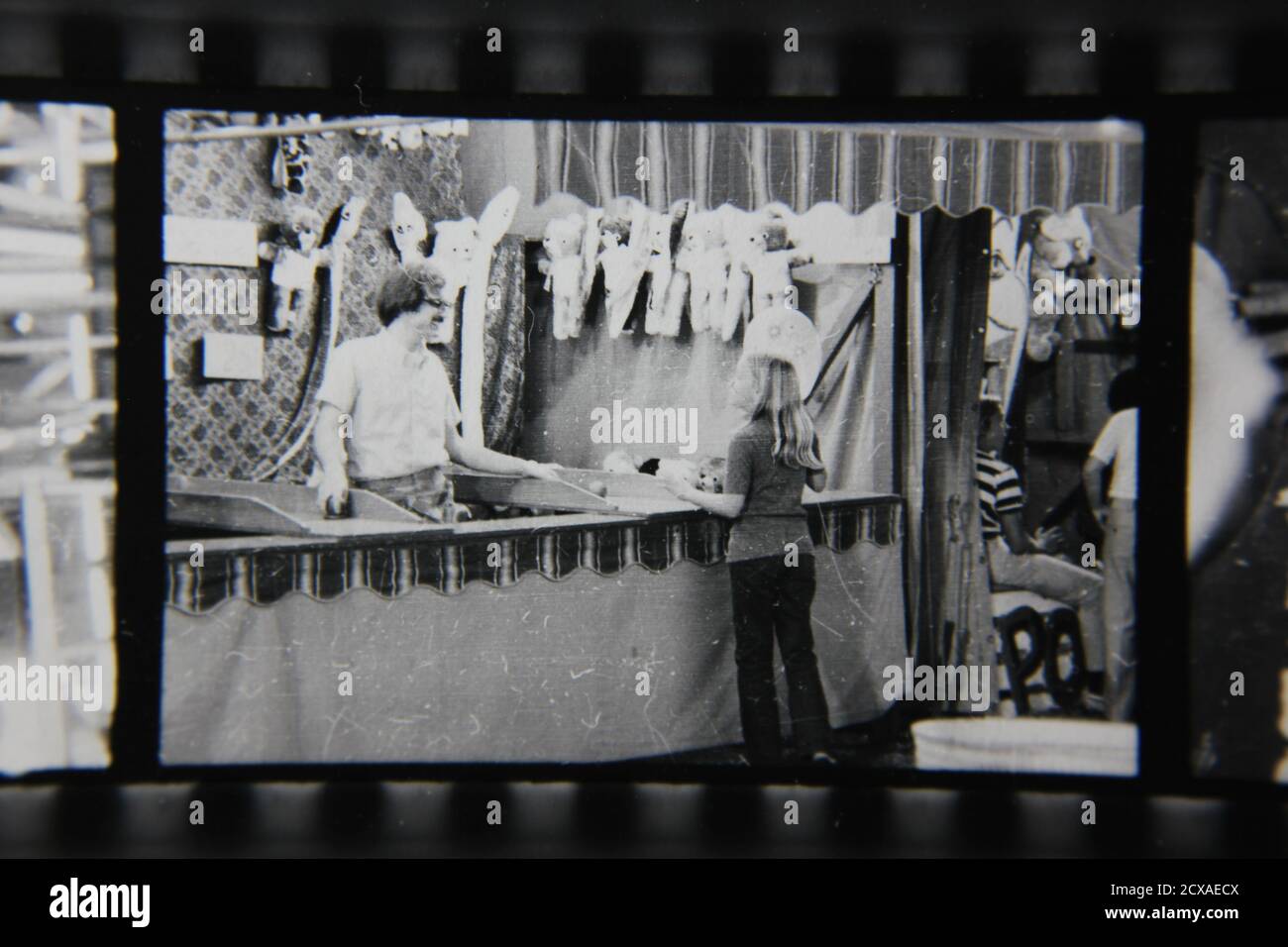 Fotografía en blanco y negro de la cosecha de los años 70 de un tipo regular que manning un puesto de juego del carnaval en una feria de la calle del carnaval. Foto de stock