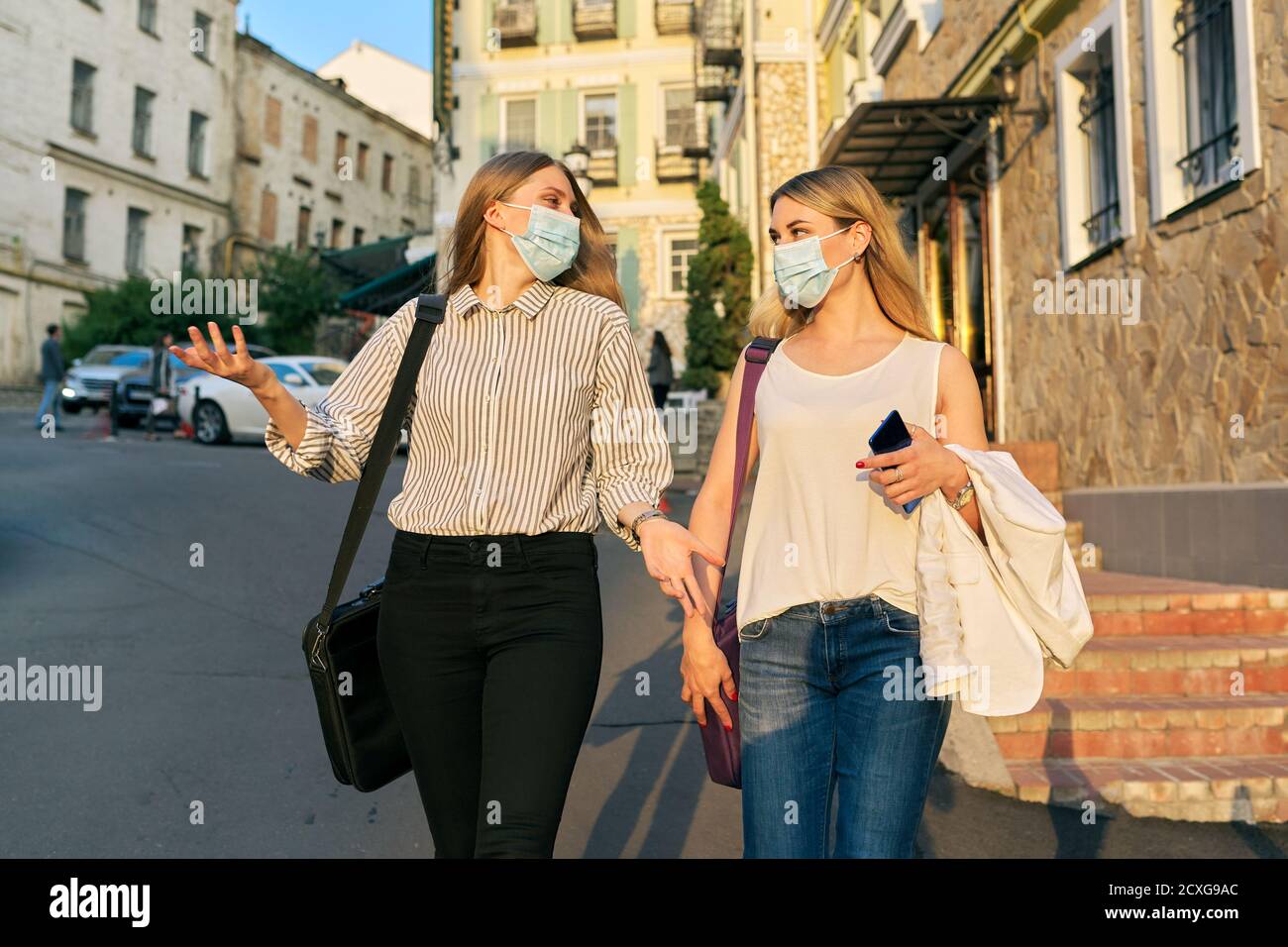 Trabajadoras de oficina dos mujeres caminando, usando máscaras de protección médica Foto de stock