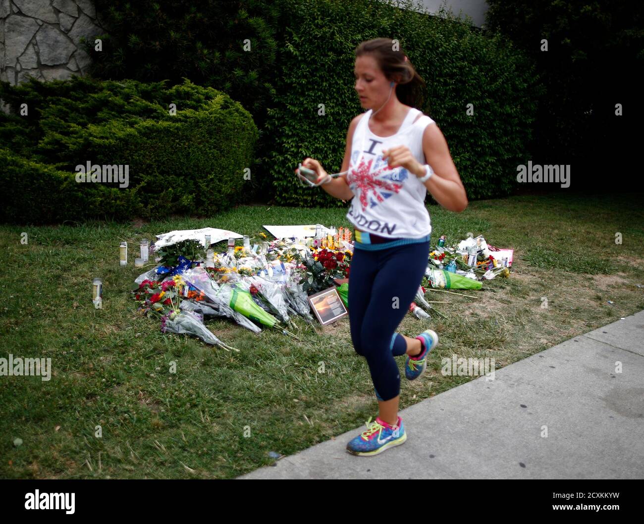A woman jogs past a makeshift memorial in front of the Alpha Phi sorority house where two women were killed in the Isla Vista neighborhood of Santa Barbara, California May 26, 2014. Twenty-two year old Elliot Rodger killed six people before taking his own life in a rampage through a California college town shortly after he posted a threatening video railing against women, police said on Saturday. REUTERS/Lucy Nicholson (UNITED STATES - Tags: CRIME LAW) Foto de stock