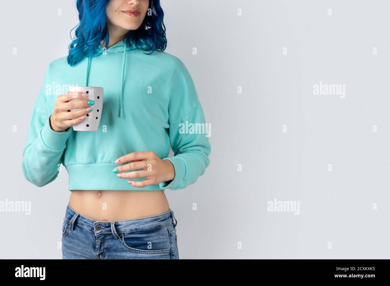 Hermosa mujer joven adulta en una sudadera con capucha de color turquesa con una taza en la mano Fotografía de stock Alamy