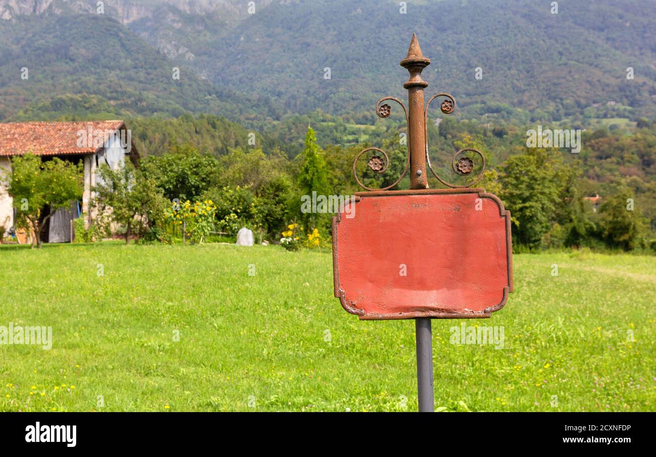 Viejo y oxidado clásico de hierro forjado en blanco signo en el medio de un prado en un paisaje rural de montaña Foto de stock