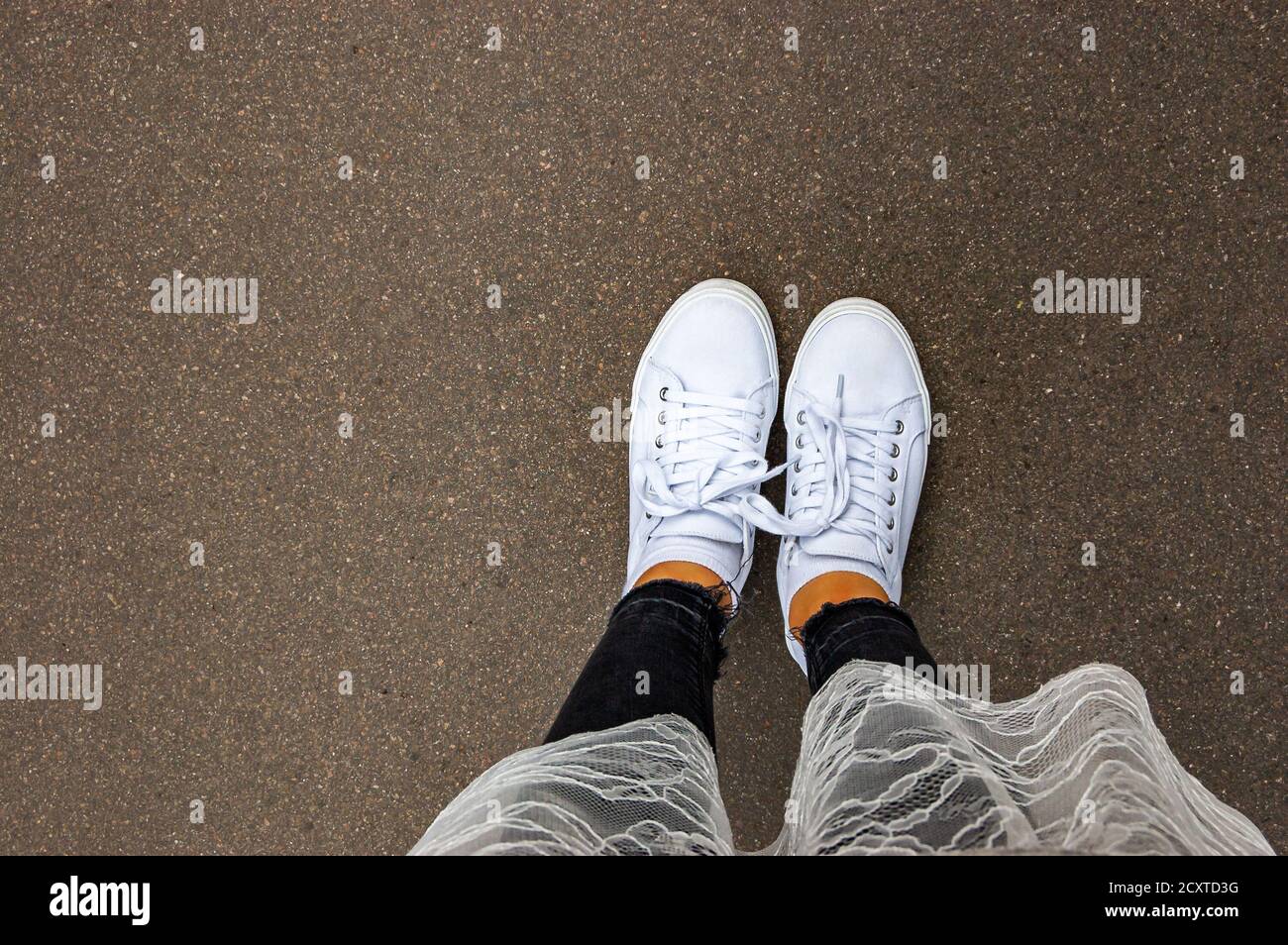 Mirando hacia abajo en zapatos blancos con pantalones vaqueros negros y  falda blanca Fotografía de stock - Alamy