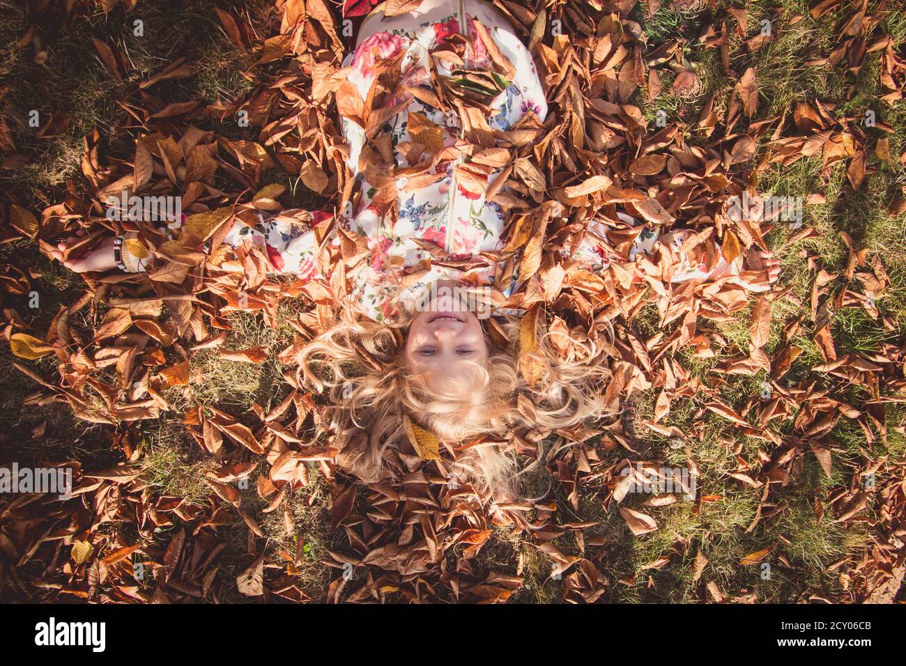 vista desde la perspectiva del ojo de los pájaros a la hermosa rubia niña que yace entre las hojas en el día soleado Foto de stock