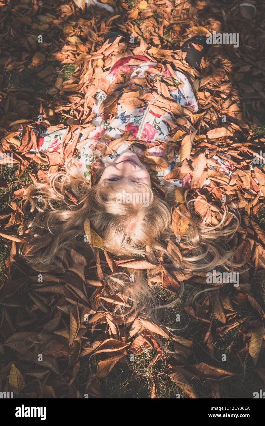 vista desde la perspectiva del ojo de los pájaros a la hermosa rubia niña que yace entre las hojas en el día soleado Foto de stock