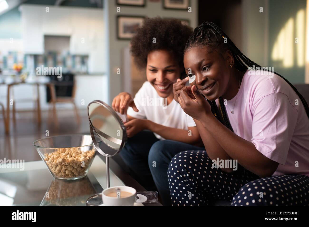 Mujeres negras felices mirando el espejo mientras se aplican los parches de los ojos en fiesta de pijamas Foto de stock
