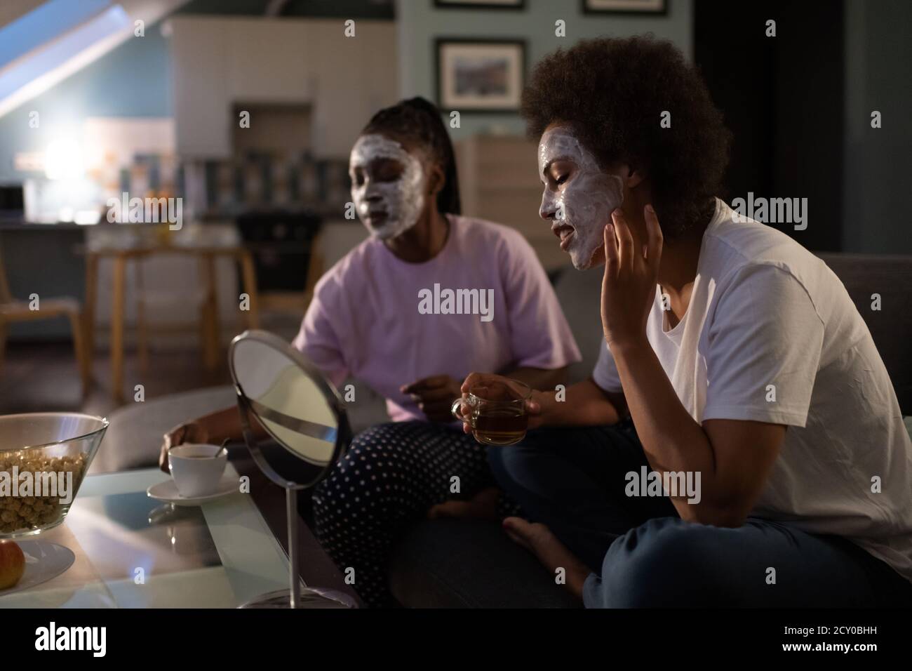 Mujer negra aplicando crema en la cara durante la fiesta de pepino con amigo en casa Foto de stock