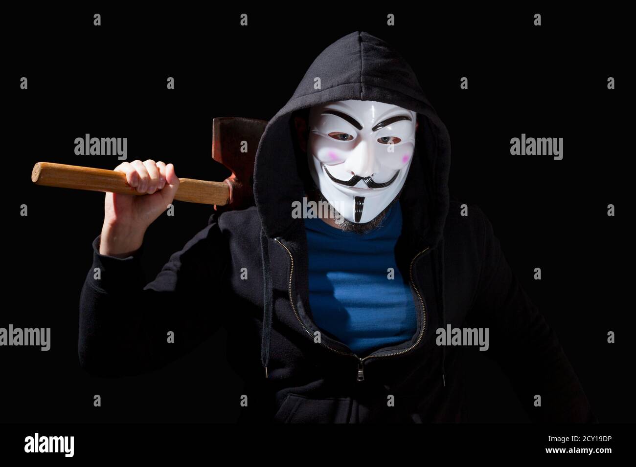 Hombre armado con un hacha y con una máscara y una sudadera con capucha sobre fondo negro. Foto de stock