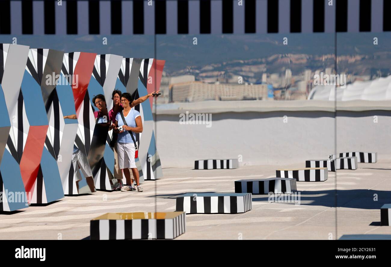 Visitors are reflected in a creation as part of the exhibition "Defini Fini Infini, Travaux in situ" by French artist Daniel Buren at the MaMo art center in Marseille September 12, 2014. The MaMo contemporary art center is installed on the restored rooftop terrace of Le Corbusier's 1947 Cite Radieuse (Radiant City) and created by French designer Ora-Ito. The exhibition will run until September 30, 2014. REUTERS/Jean-Paul Pelissier (FRANCE - Tags: ENTERTAINMENT SOCIETY) Foto de stock