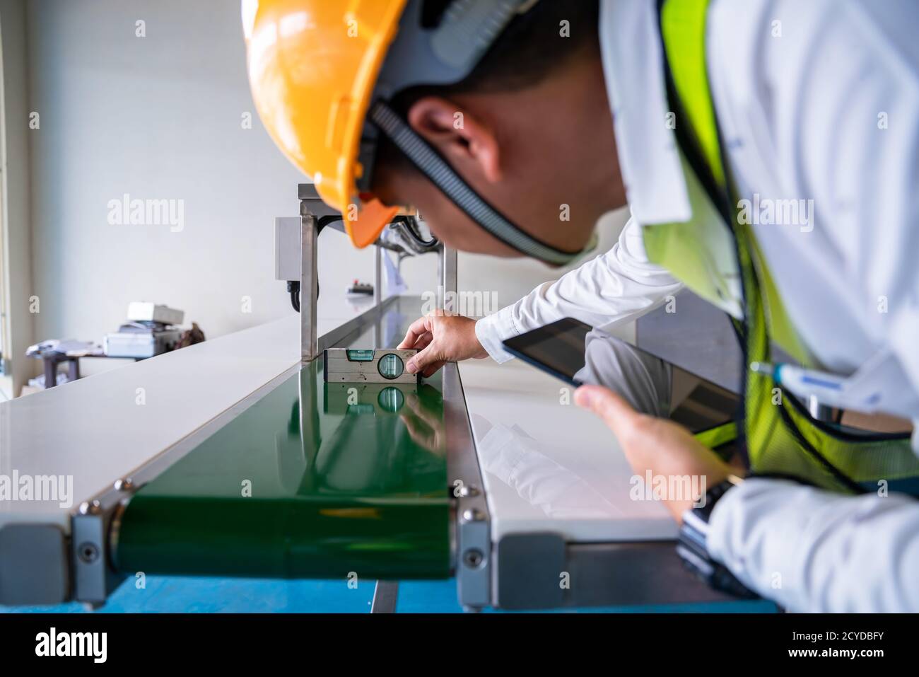 Hombre asiático mecánico técnico trabajador utiliza un medidor de nivel de agua trabajando y montar el transportador de máquina de clasificación de productos en la fábrica industrial. Foto de stock