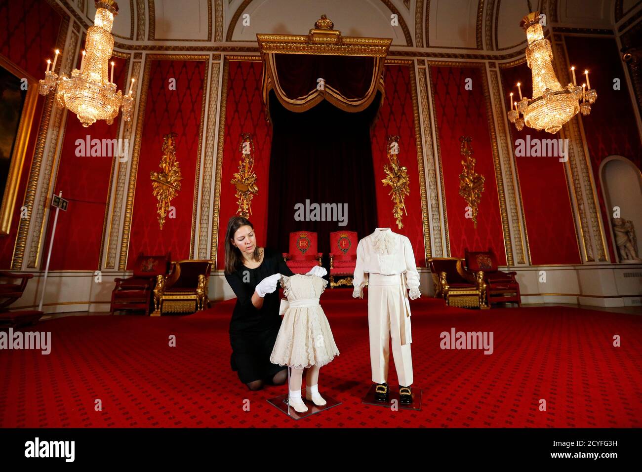 Curator Caroline de Guitaut poses in the throne room at Buckingham Palace  with the outfits worn by Britain's Princess Anne and Prince Charles (R) on  the day of their mother Queen Elizabeth's