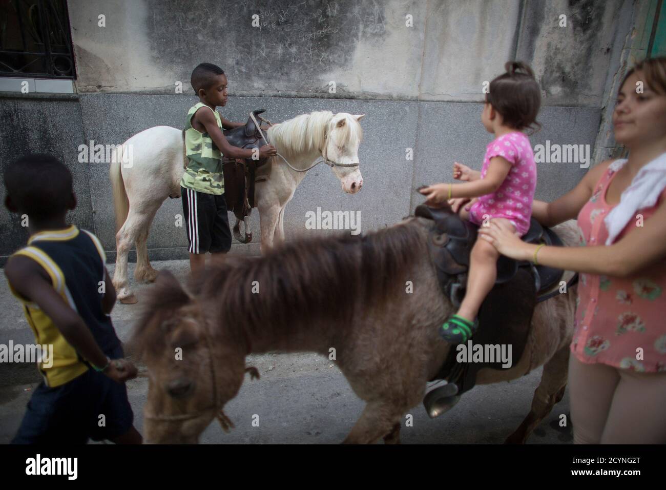 Lázaro Perez (2da L), 12, sostiene a Coco, un pony de dos años, como su hermano IRE Perez (L), de 9 años, toma el Guapo ('la hermosa' en español), un pony de cuatro años, para un rápido viaje con un niño en el centro de la Habana, 6 de marzo de 2015. La familia de Pérez dice que hacen alrededor de $15 al día, alquilando cinco ponis a niños para paseos rápidos. REUTERS/Alexandre Meneghini (CUBA - Tags: ANIMALES DE LA SOCIEDAD) Foto de stock