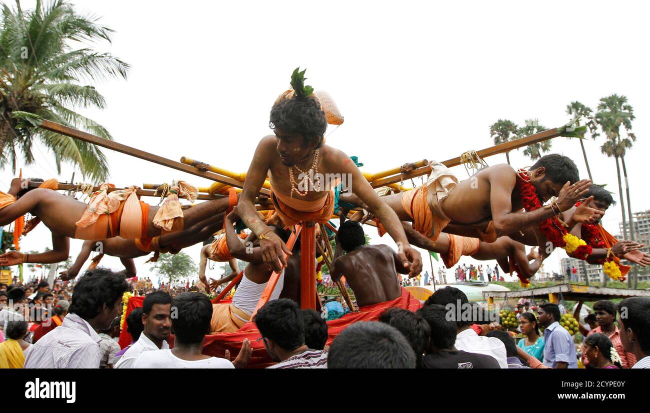 Hindu devotees hang from wooden poles using hooks pierced through their