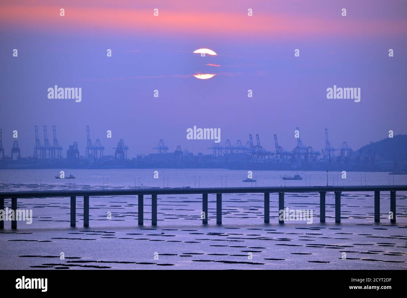 Puente de la Bahía de Shenzhen cruzando Deep Bay (后海灣), la frontera entre Hong Kong y Shenzhen, China, durante la puesta de sol con las terminales de contenedores de Shekou Foto de stock
