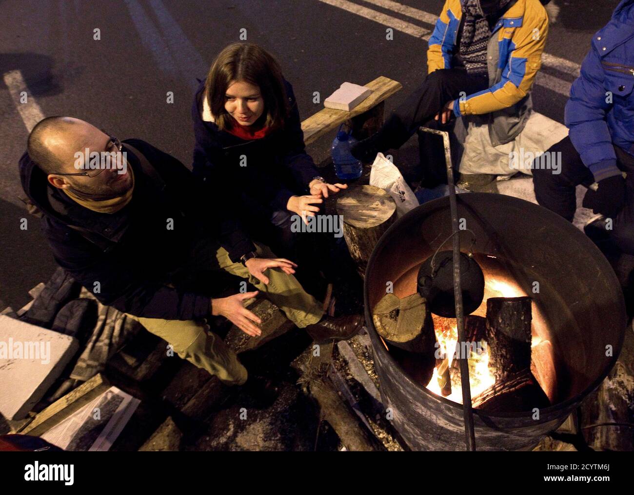 Igor Skliarevsky and his wife Elena warm themselves at a fire in a pro-European protesters camp at Independence Square in Kiev, December 16, 2013. By day, Igor Skliarevsky works as a graphic designer. By night, he is an anti-government protester, sometimes manning the barricades in Ukraine's snowy capital. The 36-year-old delivers maps for fellow protesters, directing them to medical posts or kitchens. He also set up a website coordinating food, warm clothing and other supplies for those camped out on Kiev's Independence Square. Picture taken December 16, 2013. REUTERS/Vasily Fedosenko (UKRAI Foto de stock