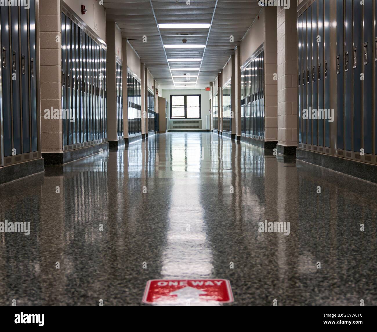 Un pasillo vacío de la escuela secundaria con una señal de sentido grabado en el piso como parte de la neew normal para abrir las escuelas en una pandemia. Foto de stock