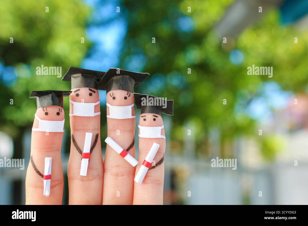 Arte de los dedos de los estudiantes en máscara médica de COVID-2019. Graduados que tienen su diploma después de graduarse. Foto de stock