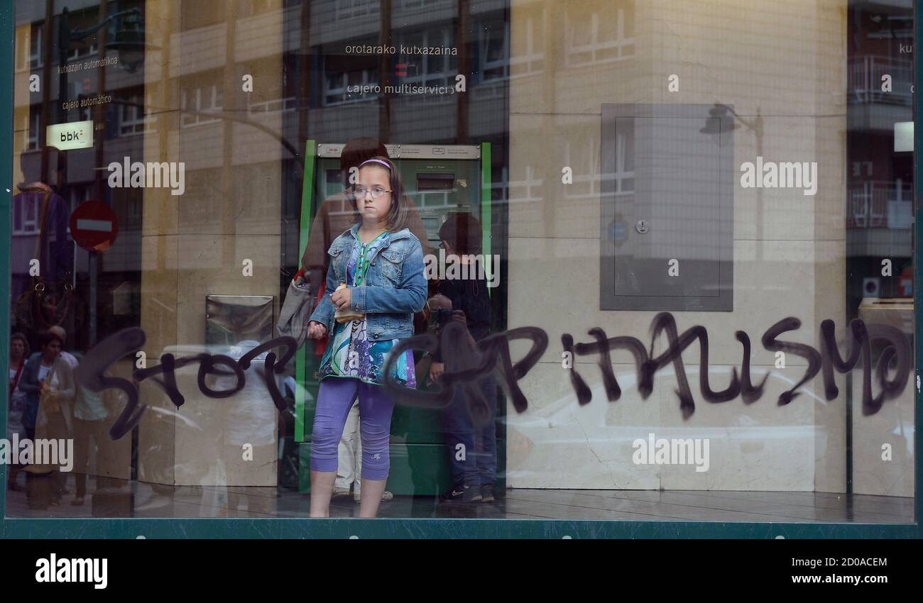 A girl looks out of a bank window sprayed with graffiti that reads, "Stop Capitalismo" in Bilbao June 7, 2012. A group of masked youths sprayed banks and estate agents with graffiti and broke windows on Thursday in the Santutxu neighbourhood of Bilbao. REUTERS/Vincent West (SPAIN - Tags: CIVIL UNREST BUSINESS) Foto de stock