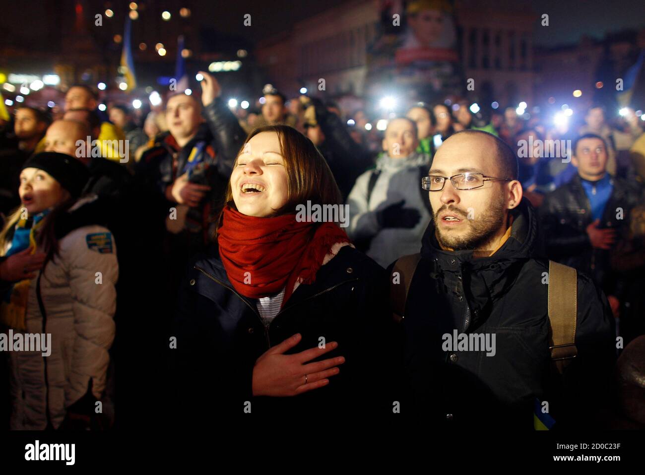 Igor Skliarevsky y su esposa Elena cantan el himno nacional durante una reunión pro-europea en la Plaza de la Independencia en Kiev, el 17 de diciembre de 2013. De día, Igor Skliarevsky trabaja como diseñador gráfico. Por la noche, es un manifestante anti-gubernamental, a veces manejando las barricadas en la capital nevada de Ucrania. El joven de 36 años entrega mapas para los compañeros manifestantes, dirigiéndolos a puestos médicos o cocinas. También creó un sitio web que coordinaba alimentos, ropa de abrigo y otros suministros para los acampados en la Plaza de la Independencia de Kiev. Foto tomada el 17 de diciembre de 2013. REUTERS/Vasily Fedosenko (UCRANIA - Foto de stock