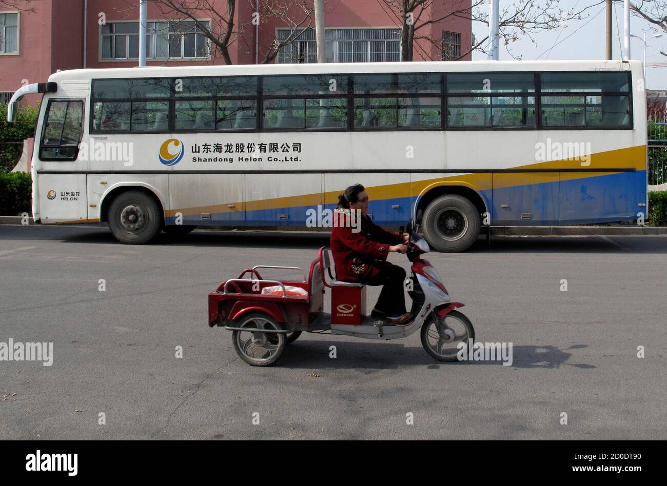 Una mujer viaja en un triciclo eléctrico pasando por un autobús de Shandong  Helon Co. Ltd. En Weifang, provincia de Shandong en este 23 de abril de  2012 foto. El funcionario chino