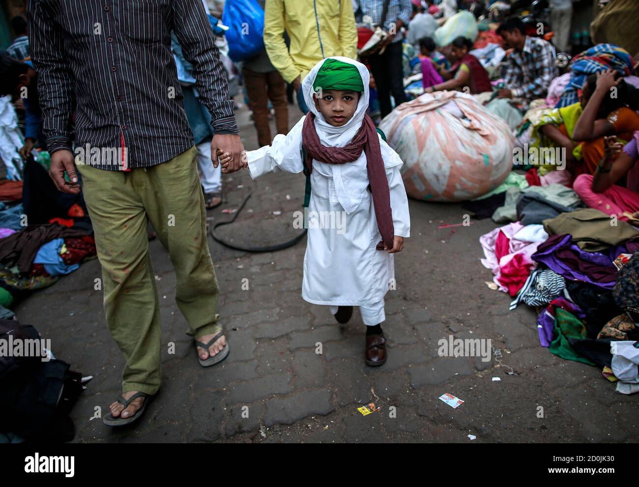 Un niño camina su padre a la escuela a través de mercado de ropa de segunda mano en Mumbai 28 de enero 2015. El mercado está abierto diariamente durante