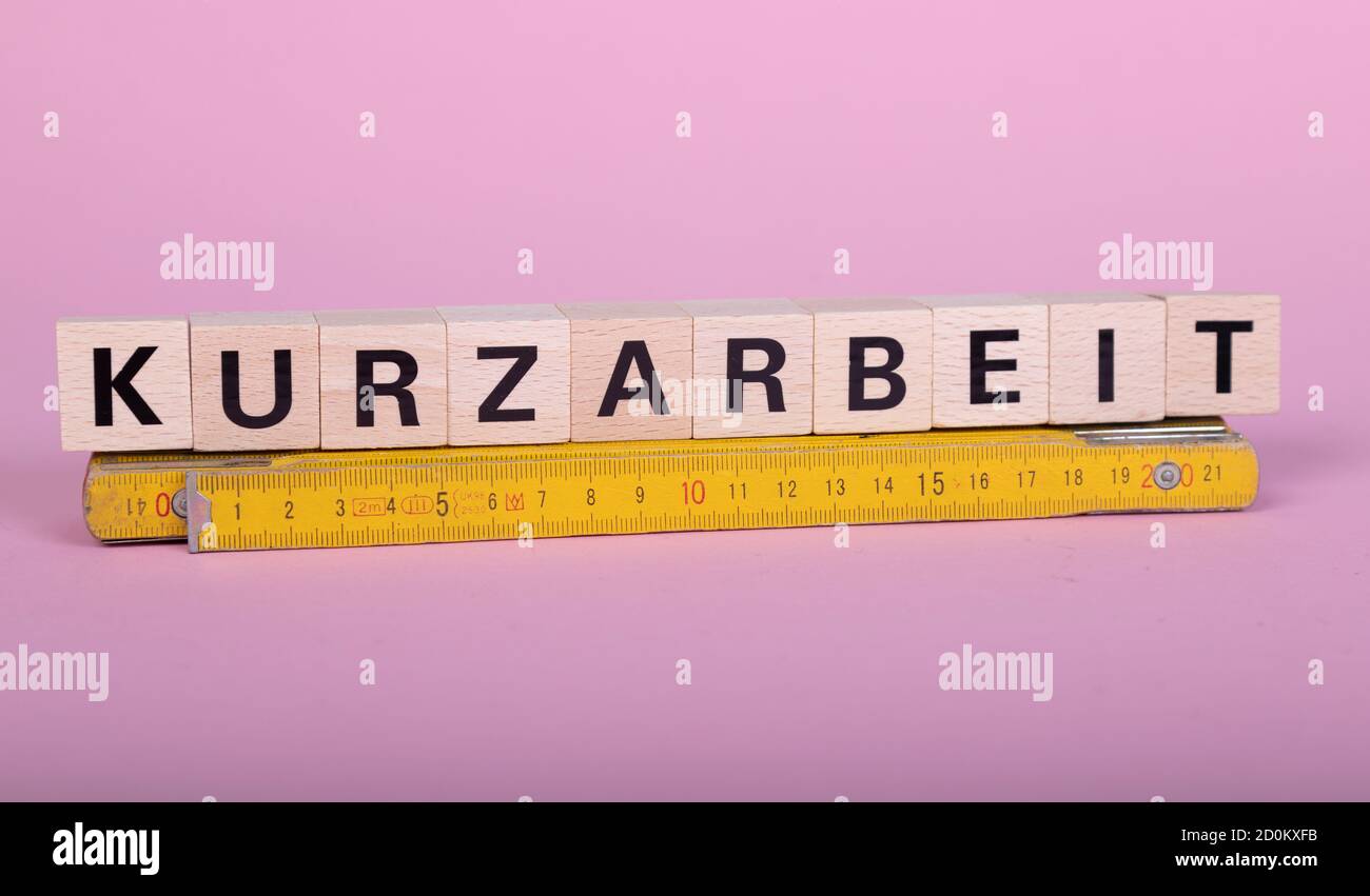 Bloques de madera con palabra alemana para trabajo de corto tiempo, Kurzarbeit, sobre una regla plegable, fondo rosa Foto de stock