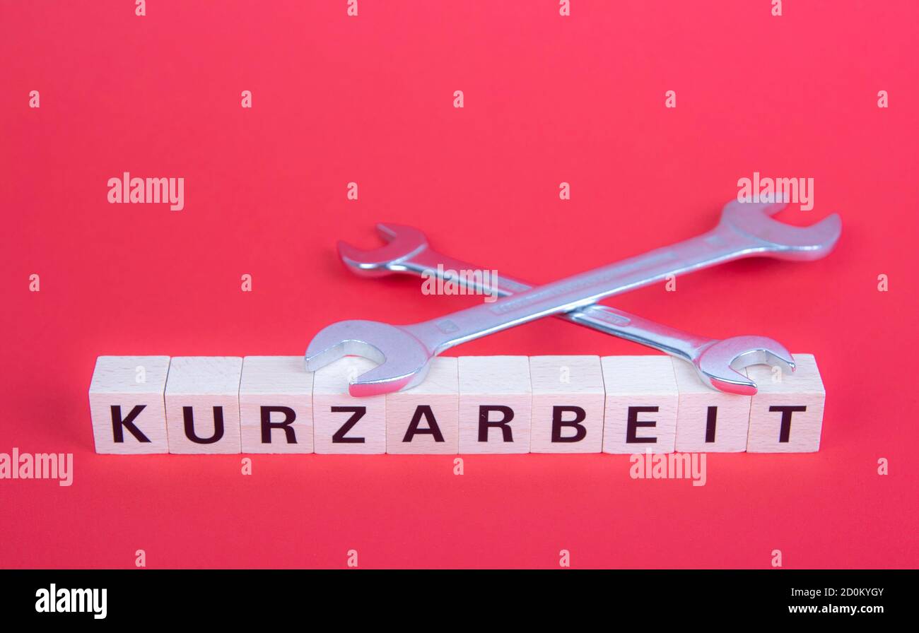 Bloques de madera con palabra alemana para trabajo de corto tiempo, Kurzarbeit, sobre dos llaves, fondo rojo Foto de stock
