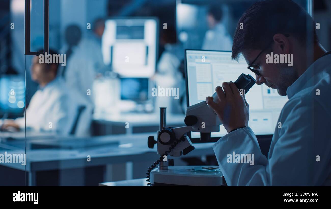 En el Laboratorio de Investigación Tecnológica: Equipo diverso de científicos Industriales, Ingenieros, Desarrolladores se reúnen alrededor de la Mesa iluminada e inspeccionan Blueprints Foto de stock
