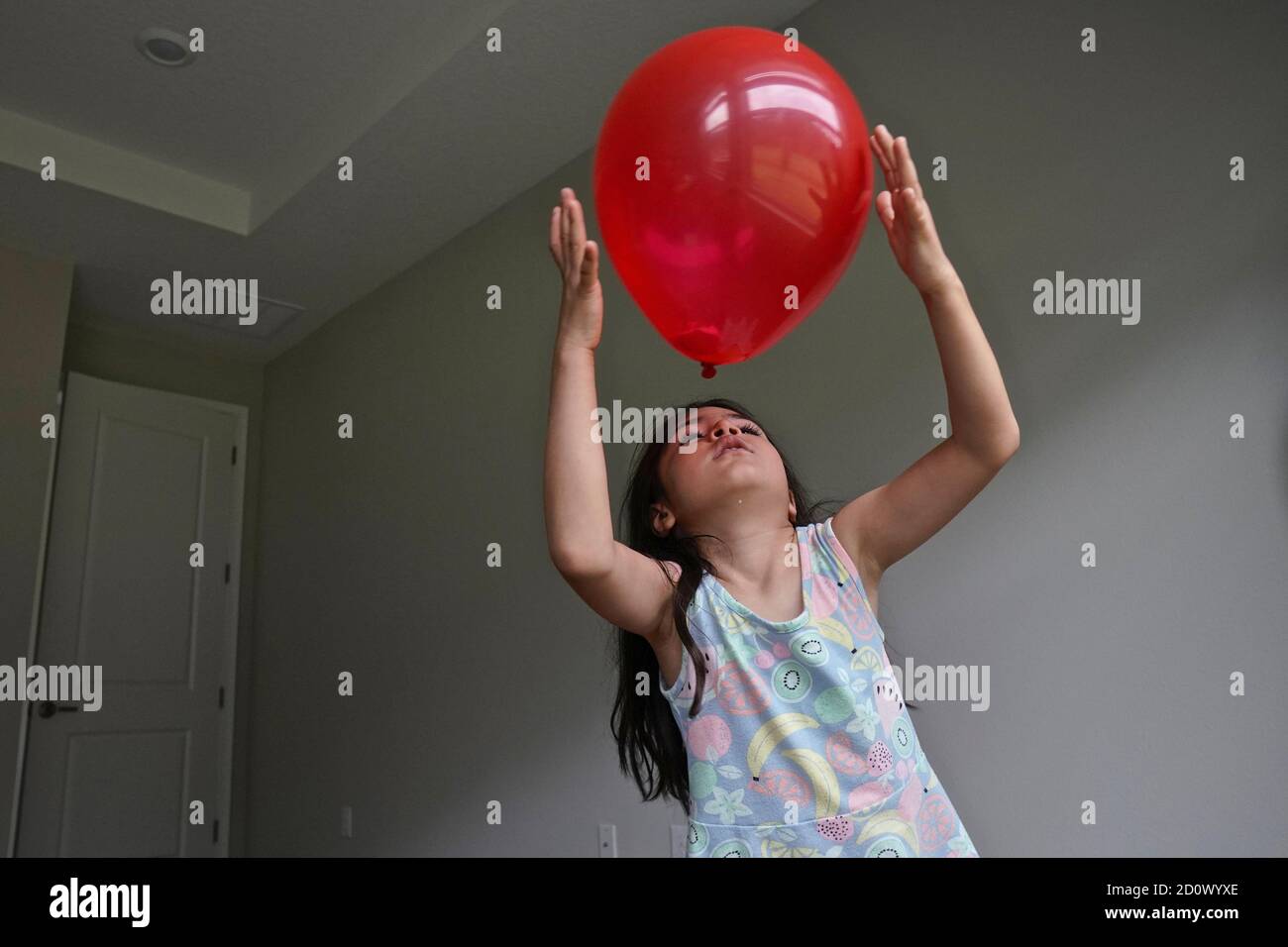 Niña de cinco años jugando con un globo rojo una habitación vacía Foto de stock