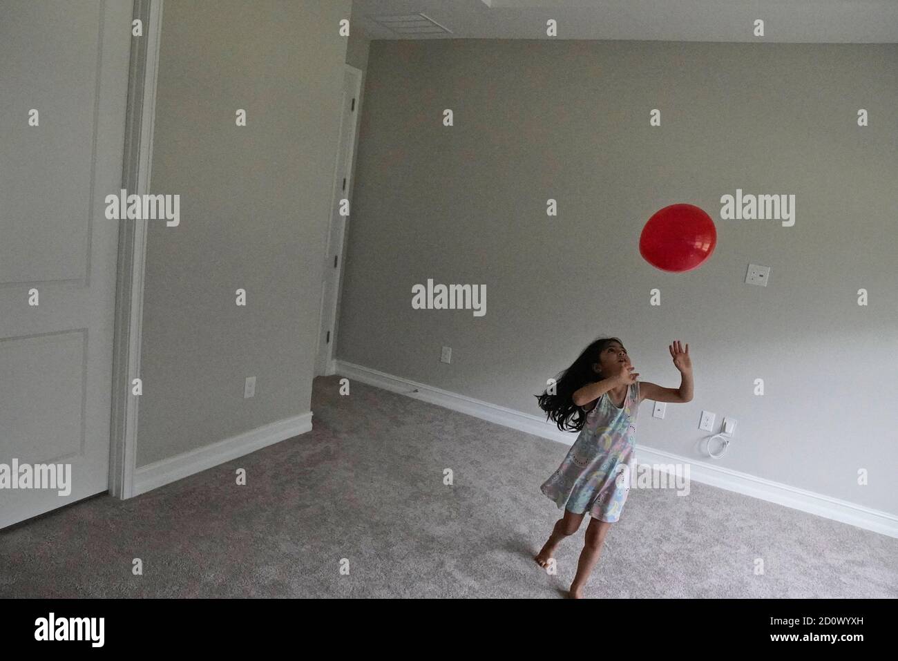 Niña de cinco años jugando con un globo rojo una habitación vacía Foto de stock