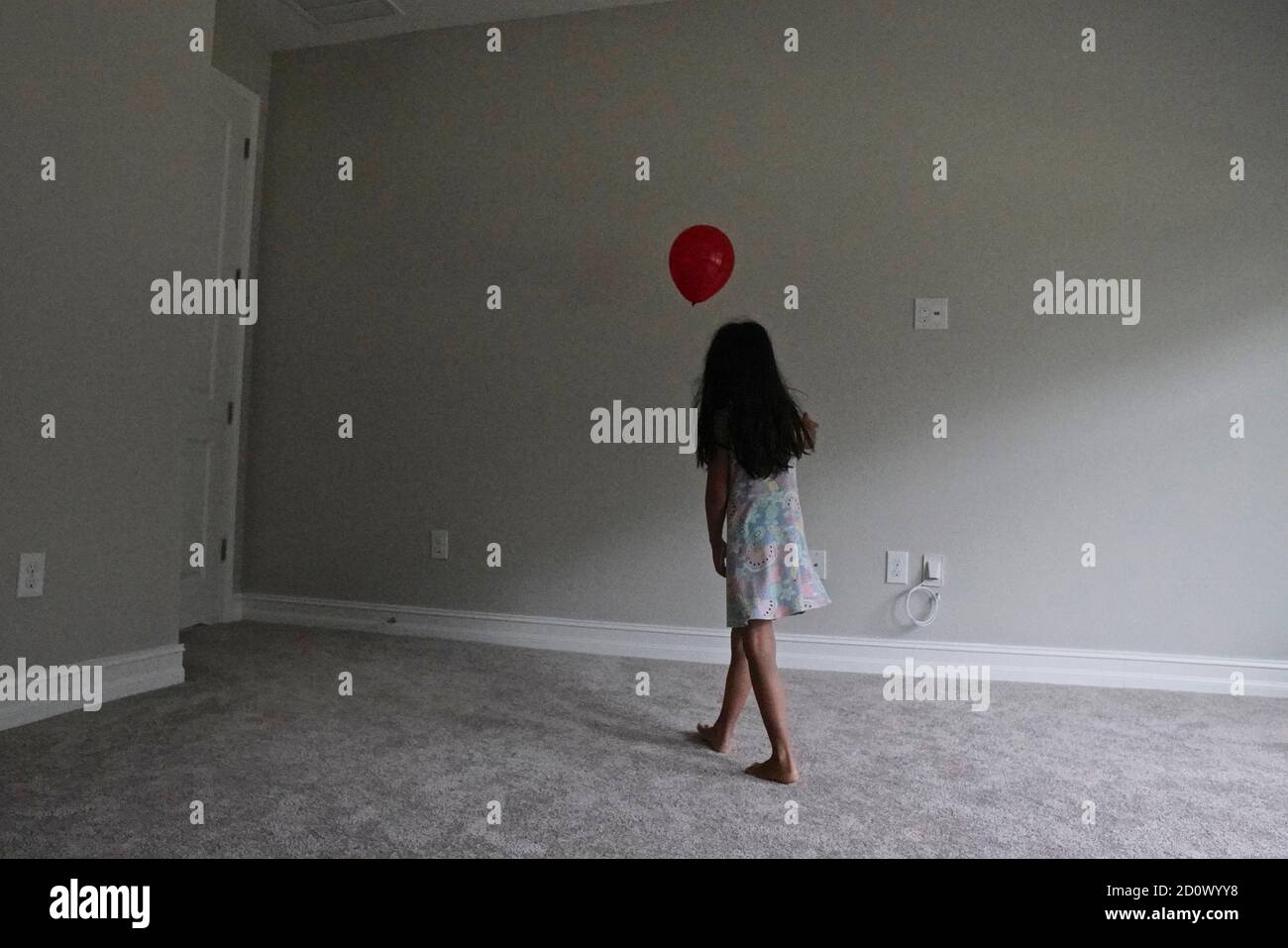 Niña de cinco años jugando con un globo rojo una habitación vacía Foto de stock