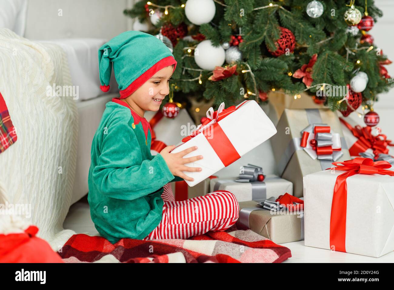 Boy abrir los regalos bajo el árbol de Noël en mañana. Niñito muchacho  sentado en el suelo abriendo regalos de Navidad. Niño bajo el árbol de  Navidad con cajas de regalo. Deco