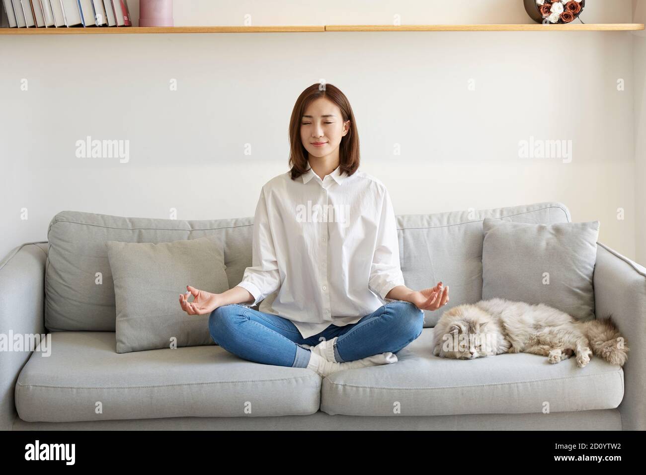 joven asiática sentada en el sofá en casa practicando yoga Foto de stock