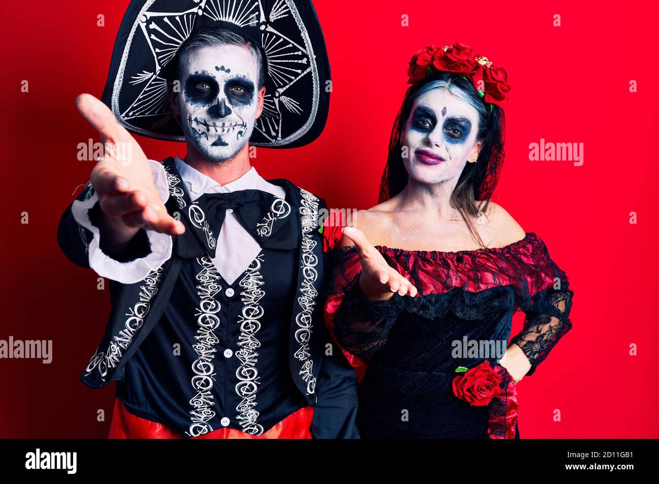 Pareja joven con el día mexicano de la muerte disfraz sobre rojo sonriente  amable ofreciendo apretón de manos como saludo y bienvenida. Negocios de  éxito Fotografía de stock - Alamy