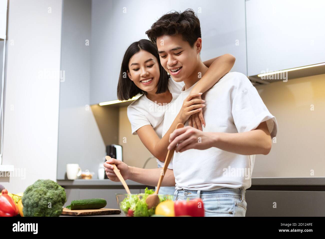 Novia asiática abrazando ensalada de cocina de novio para la cena en casa Foto de stock