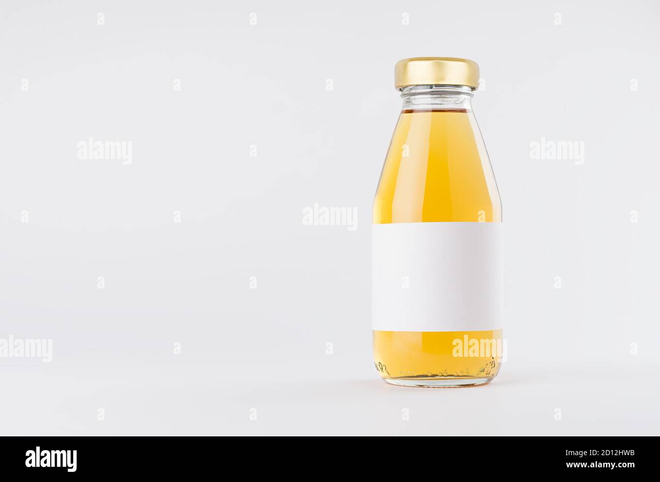 Jugo de manzana amarillo en botella de vidrio con tapón de oro y blanco etiqueta en blanco se mofa sobre fondo blanco con espacio de copia, plantilla para el embalaje, publicidad Foto de stock