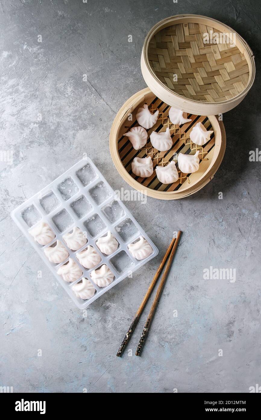 Congelados listos para cocinar asiático dumplings potstickers rellenos de  camarones en una caja de plástico con los palillos y la vaporera de bambú  más textura gris de fondo. A Fotografía de stock -