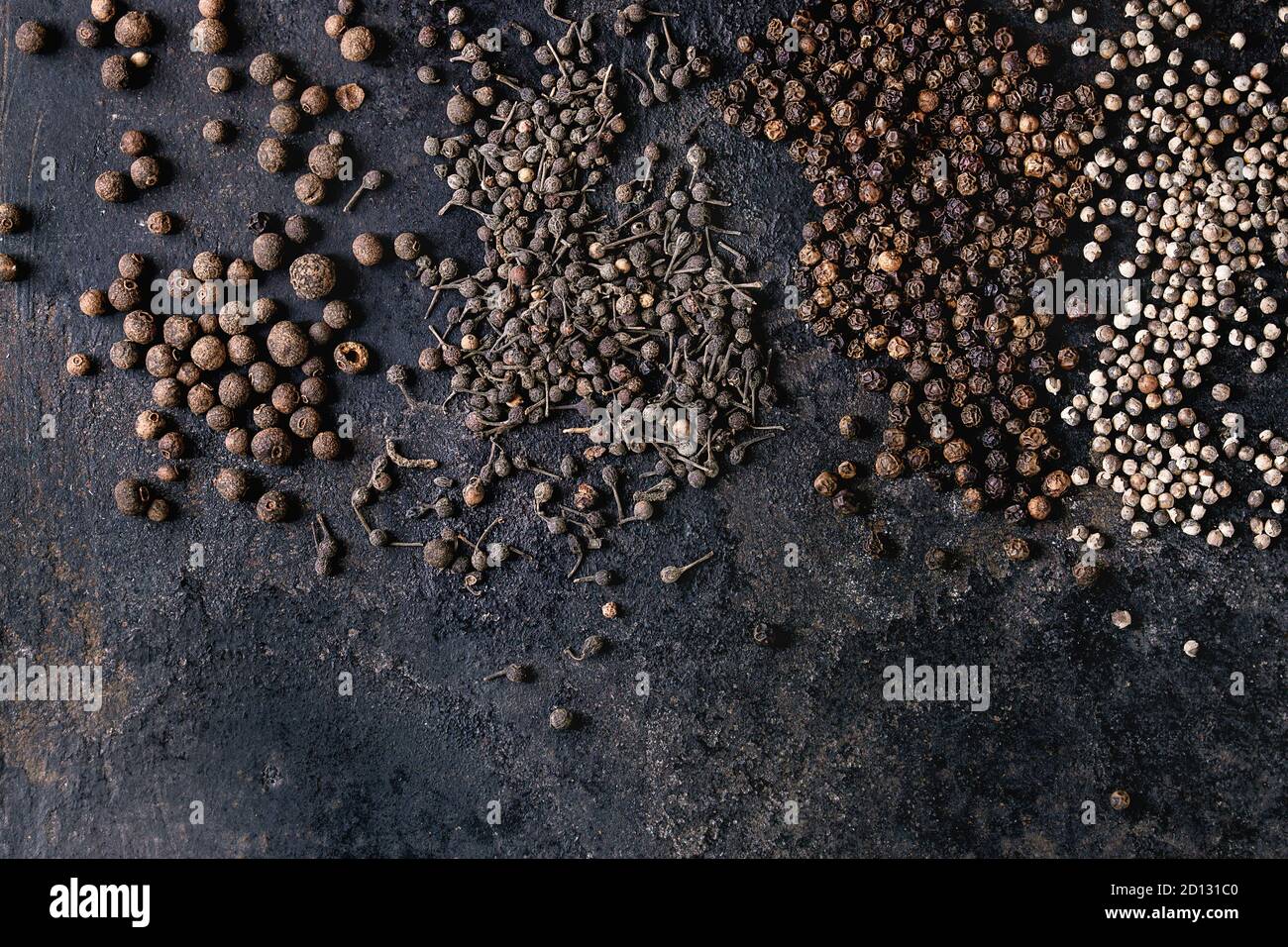 Variedad de pimiento negro pimienta de Jamaica, pimiento, monjes, los granos de pimienta pimienta negra de hierro antiguo sobre la textura de la superficie. Fondo de alimentos. Vista superior, el espacio. Foto de stock