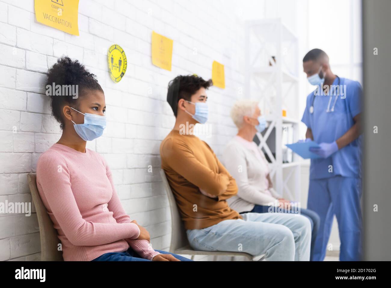 Pacientes en espera de la vacunación Covid-19 sentados en cola en el hospital Foto de stock
