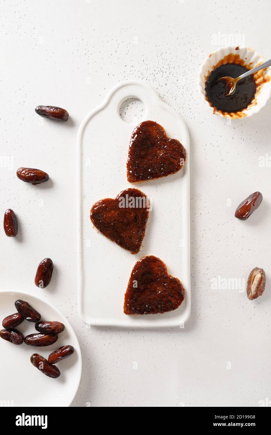 Tostadas frescas en forma de corazón con dátiles mermelada sin azúcar para un delicioso desayuno sobre mesa blanca. Vista desde arriba. Foto de stock