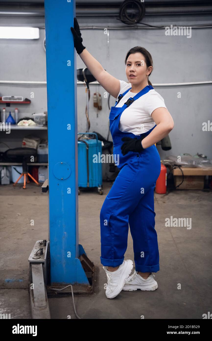 Una mujer en un mono azul está pie en taller y mirando la cámara Fotografía stock - Alamy