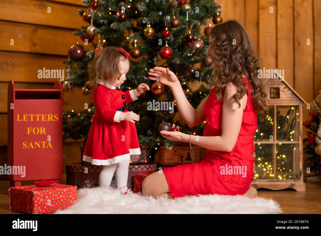 Fabulosas vacaciones de Navidad mamá e hija vestidos rojos decoran árbol de Navidad. Unas vacaciones familiares acogedoras Fotografía de stock - Alamy