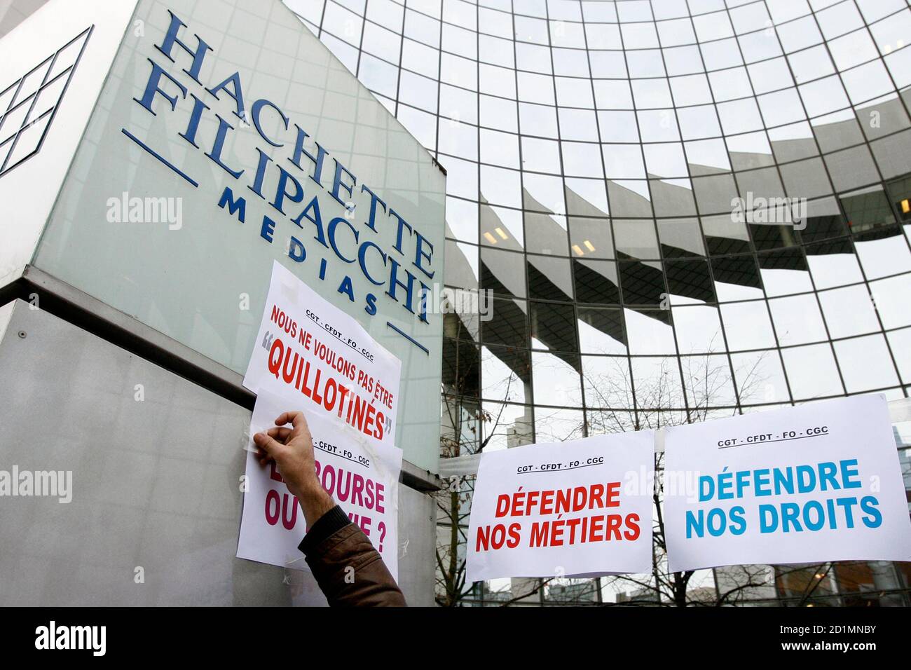 A worker of the Hachette Filipacchi Media group tapes a banner during a  demonstration against a restructuring plan of the group in front the Hachette  Filipacchi Media group building in Levallois near