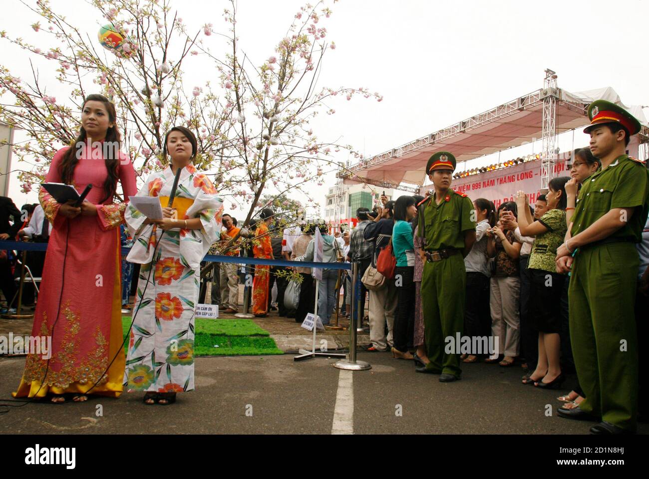 Vietnamese TV reporters wearing a traditional Vietnamese costume called 'ao  dai' (L) and a Japanese kimono stand in front of Sakura cherry blossoms  from Japan at an event to commemorate the establishment