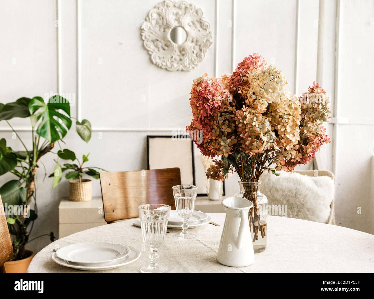 Parte del interior de la habitación. Un jarrón de flores está sobre una mesa redonda contra una pared de luz. Foto de stock