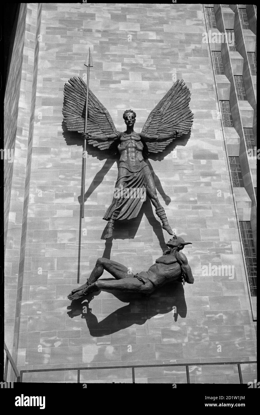 Jacob Epstein escultura de San Miguel sobre Lucifer sosteniendo una lanza larga, brazos y alas estirados, con los pies y los brazos de Lucifer atados, en el exterior de la pared del baptisterio de la nueva Catedral de San Miguel, Coventry, West Midlands, Reino Unido. Foto de stock